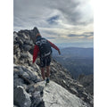 A person wearing the UltrAspire Altruist hydration pack with climbing gear while hiking along a ridge